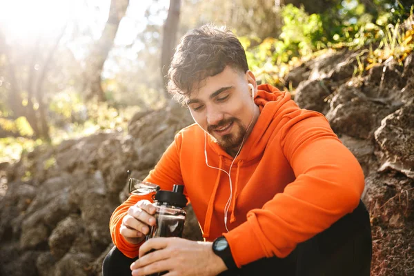 Handsome young sports fitness man runner outdoors in park drinking water. — Stock Photo, Image