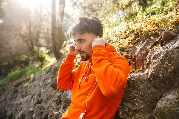 Knappe jonge sport fitness man loper buiten in park luisteren muziek met koptelefoon. — Stockfoto