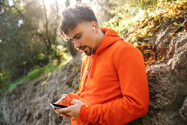 Sports fitness man runner outdoors in park listening music with earphones using mobile phone. — Stock Photo, Image