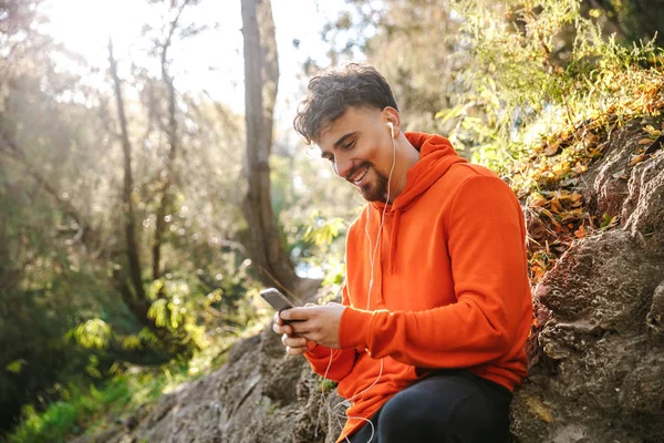 Sports fitness man runner outdoors in park listening music with earphones using mobile phone. — Stock Photo, Image