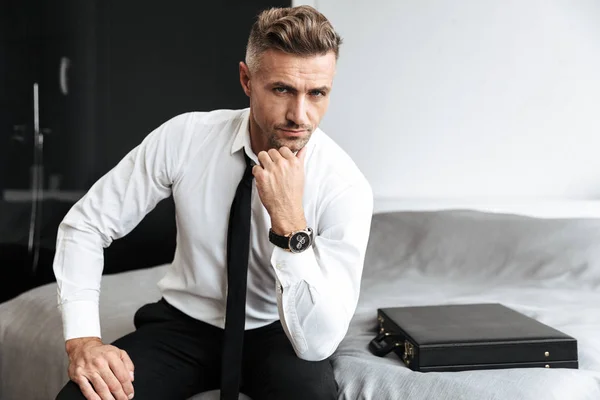 Ernster Geschäftsmann im Schlafzimmer drinnen zu Hause auf dem Bett sitzend. — Stockfoto