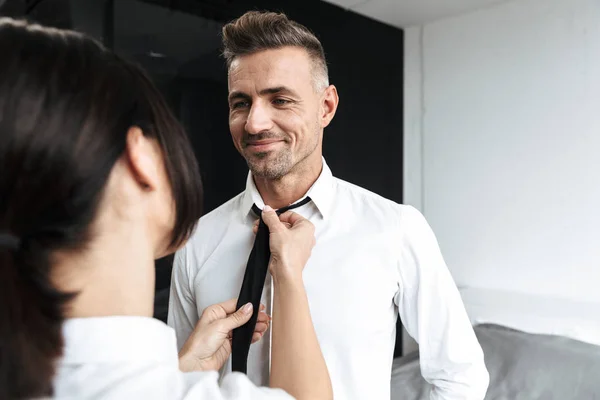 Woman help to her husband boyfriend with tie formal clothes indoors at home.