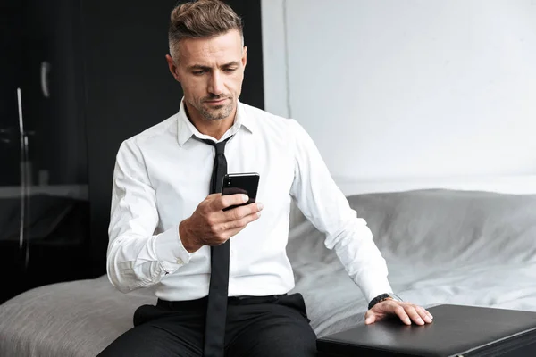 Business man in bedroom indoors at home sitting on bed using mobile phone. — Stock Photo, Image