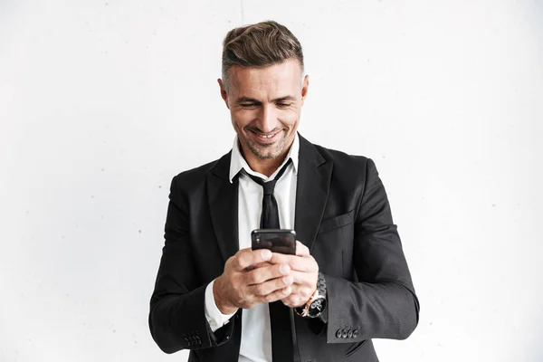 Hombre de negocios feliz posando aislado sobre fondo de pared blanca usando teléfono móvil . — Foto de Stock