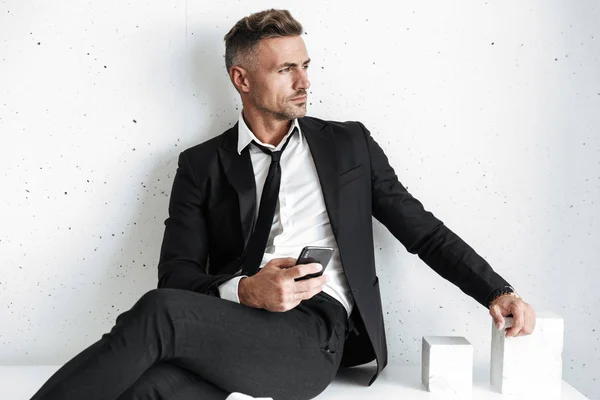 Hombre de negocios posando aislado sobre fondo de pared blanca usando teléfono móvil . — Foto de Stock