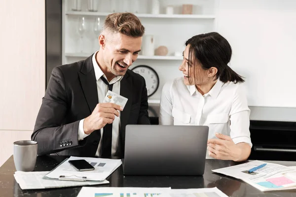 Knappe zakenman werken binnenshuis met zijn collega-vrouw met documenten en laptopcomputer. — Stockfoto