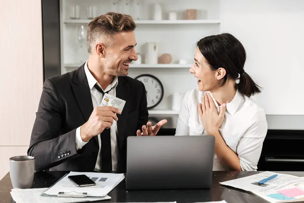 Hombre de negocios guapo trabaja en interiores con su colega mujer con documentos y computadora portátil con tarjeta de crédito . — Foto de Stock