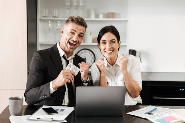 Hombre de negocios guapo trabaja en interiores con su colega mujer con documentos y computadora portátil con tarjeta de crédito . — Foto de Stock