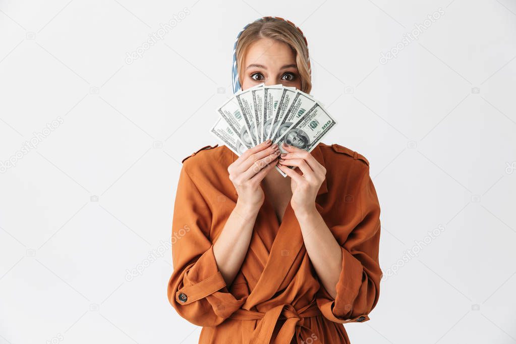 Beautiful excited young blonde pretty woman wearing silk scarf posing isolated over white wall background holding money.