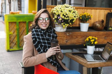Açık havada kahve içme kafede otururken dizüstü bilgisayar kullanan güzel genç kadın.