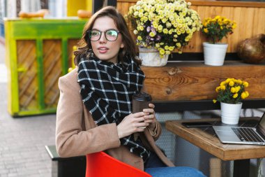 Açık havada kahve içme kafede otururken dizüstü bilgisayar kullanan güzel genç kadın.