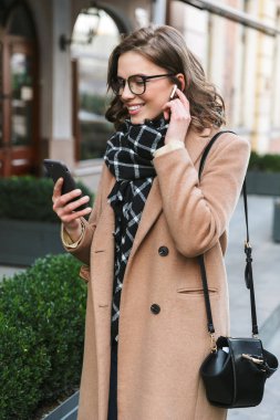 Cep telefonu dinleme müzik kulaklık kullanarak street tarafından açık havada yürüyen genç kadın.