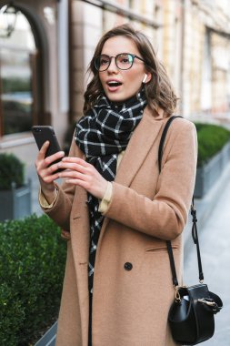 Cep telefonu dinleme müzik kulaklık kullanarak street tarafından açık havada yürüyen genç kadın.