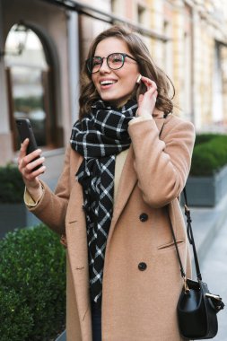 Cep telefonu dinleme müzik kulaklık kullanarak street tarafından açık havada yürüyen genç kadın.