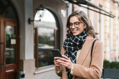 Cep telefonu dinleme müzik kulaklık kullanarak street tarafından açık havada yürüyen genç kadın.