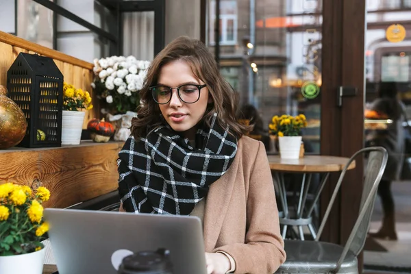 Vacker ung kvinna som använder bärbar dator sitter i café utomhus. — Stockfoto