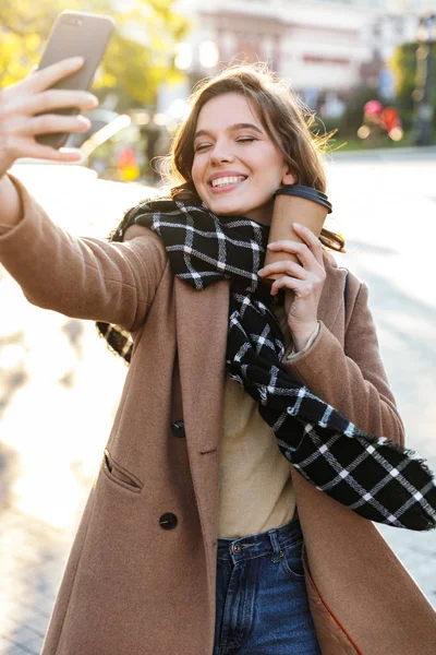 Щаслива молода жінка бере селфі по мобільному телефону на відкритому повітрі, що йде вулицею . — стокове фото
