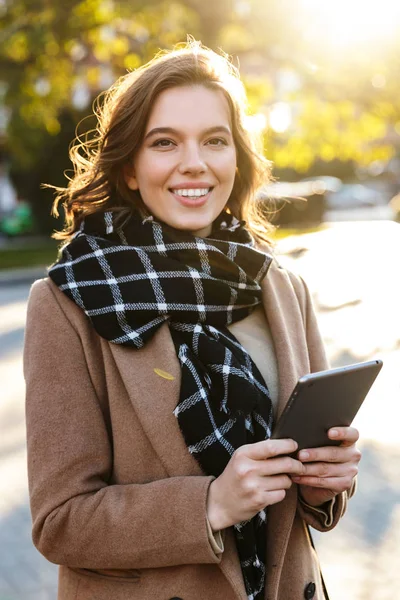 Happy young woman outdoors walking by street using tablet computer.