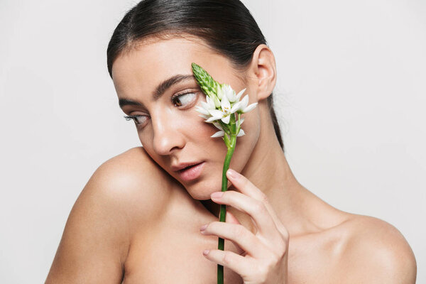 Healthy attractive brunette woman standing isolated holding flower plant near her face
