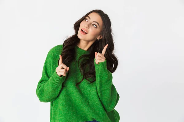 Jovem mulher vestida com suéter verde posando isolado sobre fundo da parede branca apontando . — Fotografia de Stock