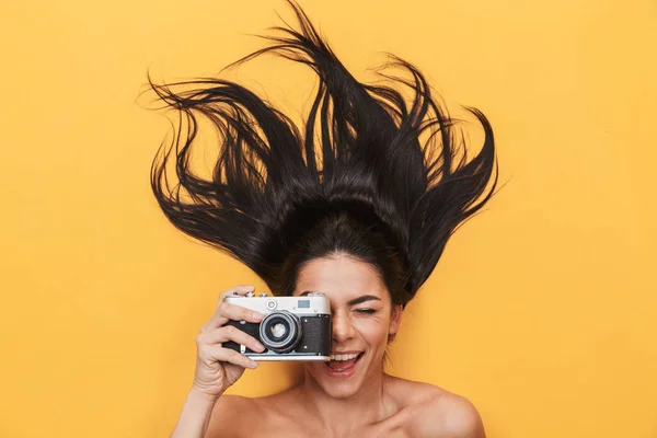 Feliz joven mujer yace aislada sobre fondo amarillo sosteniendo cámara fotográfica . — Foto de Stock