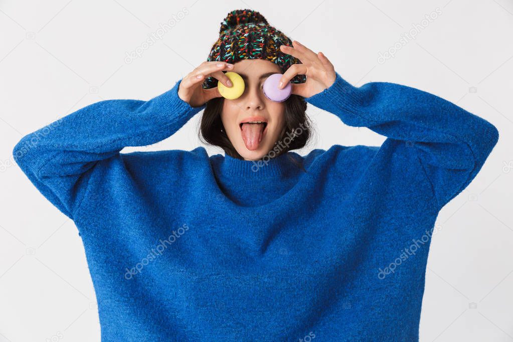 Portrait of positive woman 30s wearing winter hat holding macaro