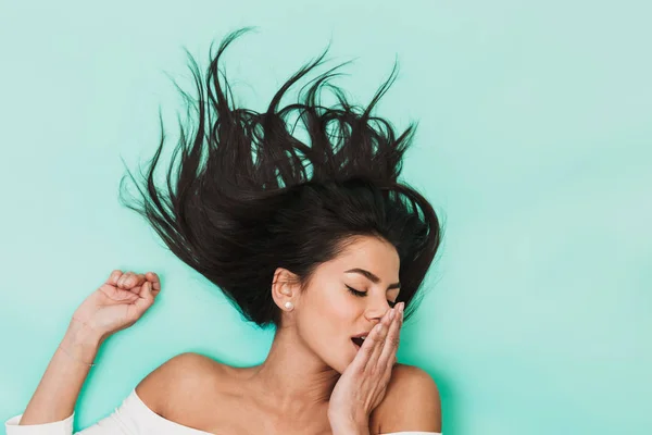 Bella sbadigliando giovane donna assonnata si trova isolata su sfondo luce blu. Concetto di capelli sani . — Foto Stock