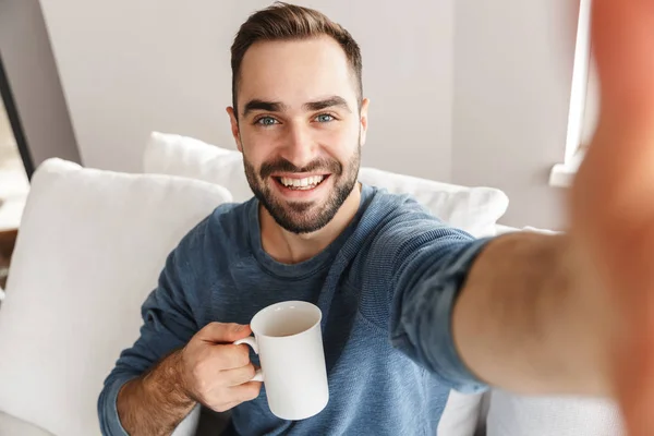 Felice giovane seduto su un divano a casa — Foto Stock