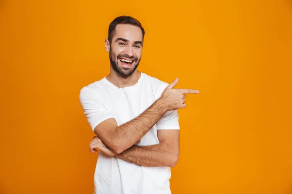 Imagem de homem barbudo de 30 anos em t-shirt apontando dedo de lado, enquanto — Fotografia de Stock