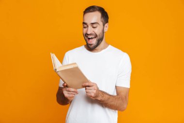 Görüntü mutlu adamın 30'lu yaşlarda beyaz t-shirt tutarak ve kitap okuma