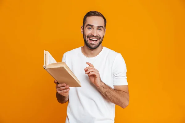 Εικόνα του άνδρα χαμογελώντας 30s σε λευκό t-shirt κρατώντας και ανάγνωση Μπο — Φωτογραφία Αρχείου