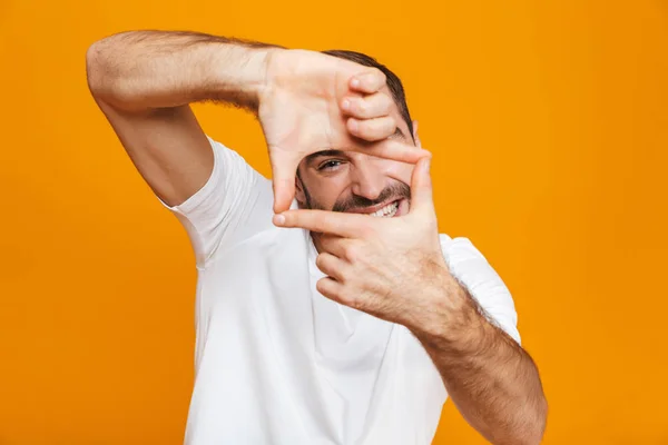 Изображение красивого 30-летнего парня в футболке, показывающего рамку с пальцами — стоковое фото