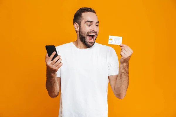 Фотографія ненадійного чоловіка 30s в повсякденному носінні тримає смартфон і — стокове фото