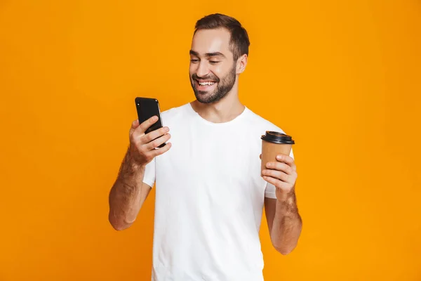 Zdjęcie z pięknego człowieka 30s w odzież codzienna, trzymając telefon komórkowy i — Zdjęcie stockowe