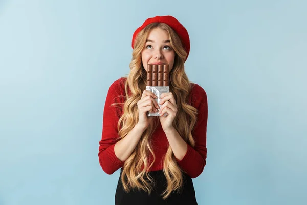 Imagem da menina loira 20s vestindo boina vermelha comendo barra de chocolate — Fotografia de Stock