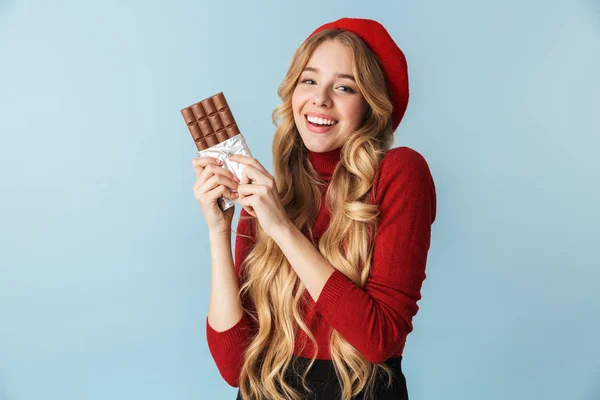 Imagem da menina sorridente 20s vestindo boina vermelha comendo barra de chocolate — Fotografia de Stock