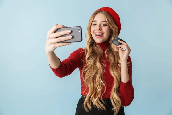 Modest blond woman 20s holding credit card while taking selfie p
