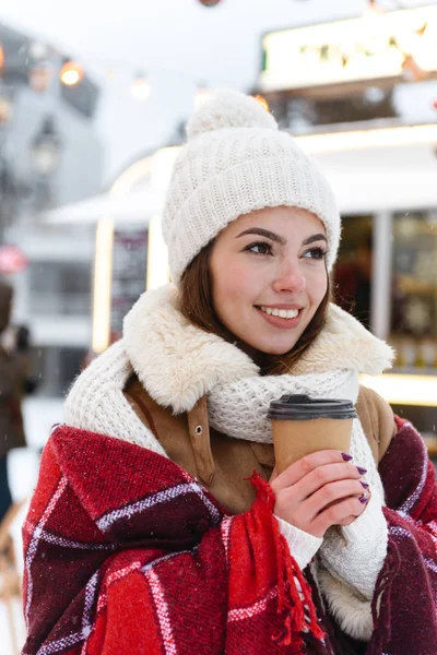 Mulher bonita em chapéu e cachecol andando ao ar livre no parque nevado rua beber café segurando xícara . — Fotografia de Stock