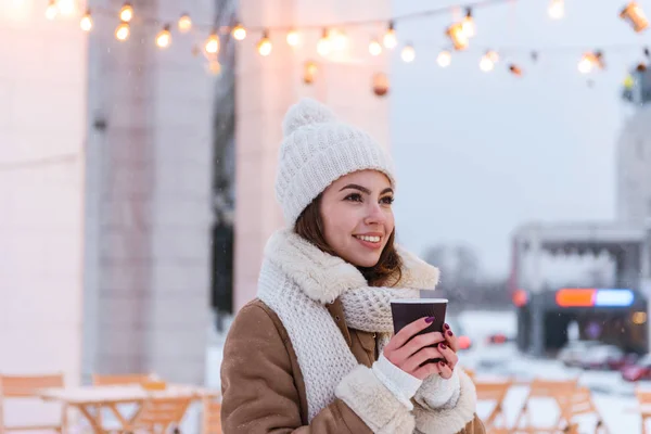 Νεαρή γυναίκα με καπέλο και κασκόλ περπάτημα σε εξωτερικούς χώρους τον χειμώνα χιόνι πίνοντας καφέ. — Φωτογραφία Αρχείου