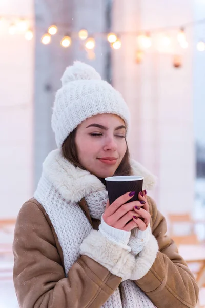 Jovem mulher de chapéu e cachecol andando ao ar livre no inverno neve beber café . — Fotografia de Stock