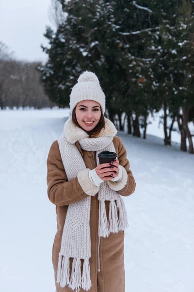 Jovem mulher de chapéu e cachecol andando ao ar livre no inverno neve beber café . — Fotografia de Stock