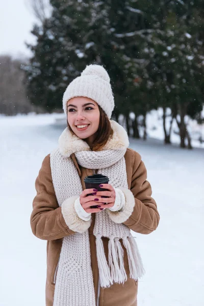 Молода жінка в капелюсі і шарфі ходить на відкритому повітрі взимку сніг п'є каву . — стокове фото