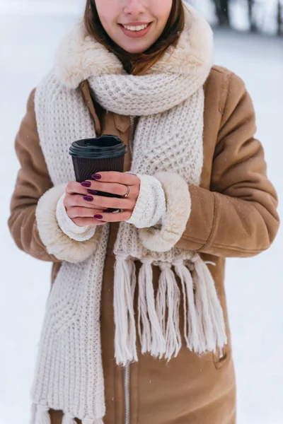 Junge Frau mit Hut und Schal, die im Winter draußen im Schnee Kaffee trinkt. — Stockfoto