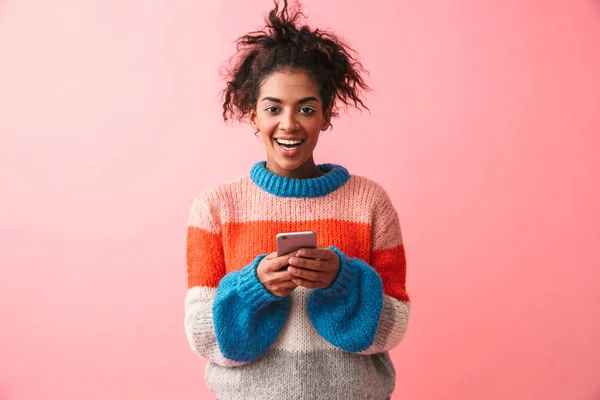 Gelukkig mooie jonge Afrikaanse vrouw poseren geïsoleerde over roze muur achtergrond met behulp van mobiele telefoon. — Stockfoto