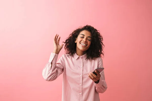Rindo jovem mulher africana posando isolado sobre fundo de parede rosa vestida em pijama usando telefone celular . — Fotografia de Stock