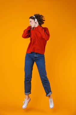 Duygusal genç güzel kadın izole kulaklık ile müzik dinleme sarı duvar arka plan üzerinde poz.