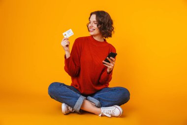 Cep telefonu kullaranarak sarı duvar arka plan üzerinde izole poz genç güzel kadın.