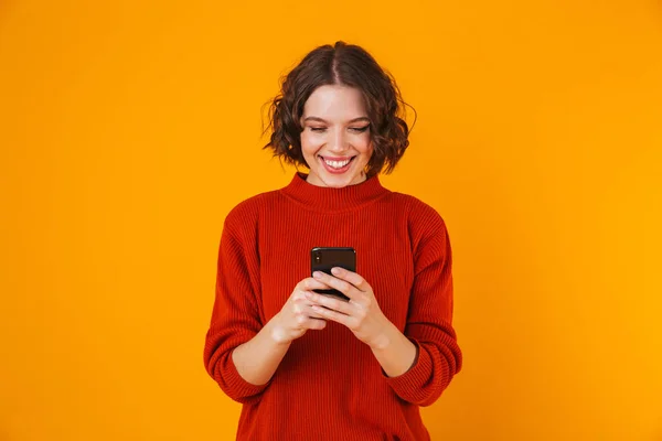 Happy young pretty woman posing isolated over yellow wall background using mobile phone. — Stock Photo, Image