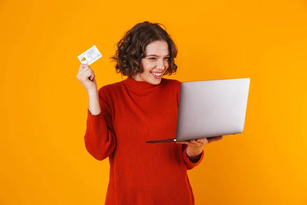 Beeld van vrolijke vrouw met zilveren laptop en creditcard terwijl — Stockfoto