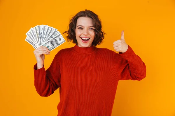 Opgewonden gelukkig jonge mooie vrouw poseren geïsoleerde over gele muur achtergrond aanhouden van geld. — Stockfoto